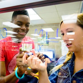 Two students writing on glass while working on project.