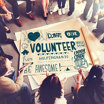 People sitting on floor around sign saying volunteer.