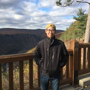Junhow Wei Asian male standing on a wooden deck overlooking mountains in the fall.